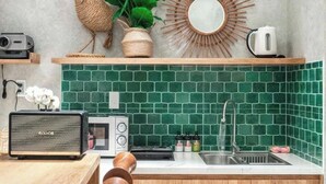 A kitchen with a green tiled backsplash, wooden cabinets, a wooden countertop, a radio, a kettle, and a decorative mirror. - HHome Tran Dinh Xu (Ho Chi Minh City)