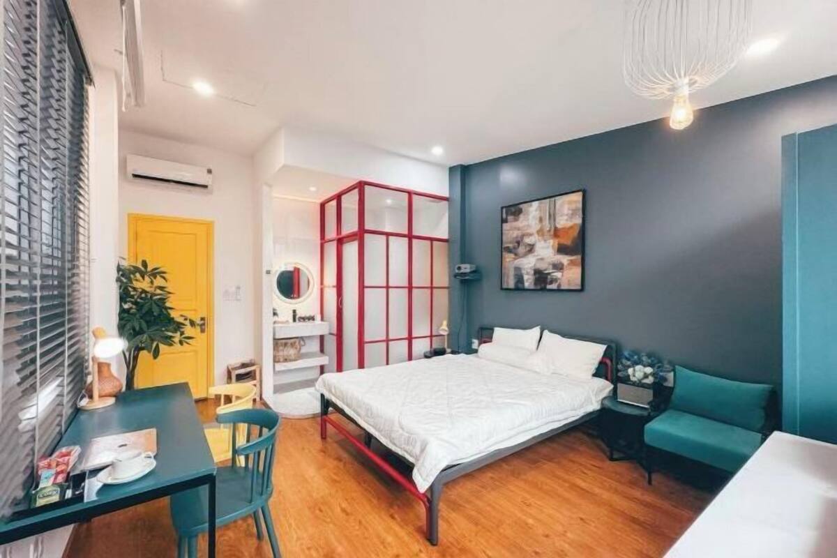 A modern bedroom with a bed, a desk, a chair, a sofa, and a red-framed wardrobe.
