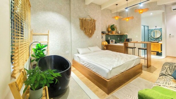 A modern bedroom with a large bed, a black bathtub, a wooden ladder, and a small kitchenette in the background. - HHome Tran Dinh Xu (Ho Chi Minh City)