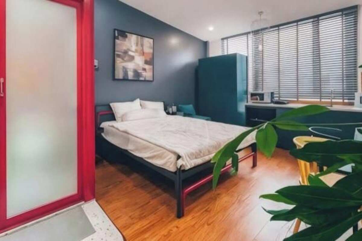 A bedroom with a bed, a desk, a chair, and a large plant.