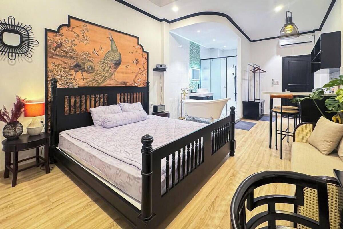 A bedroom with a bed, a desk, a chair, a sofa, a mirror, and a painting on the wall.