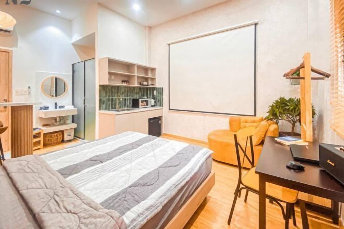 A modern bedroom with a bed, a desk, a chair, a TV, and a kitchenette.
