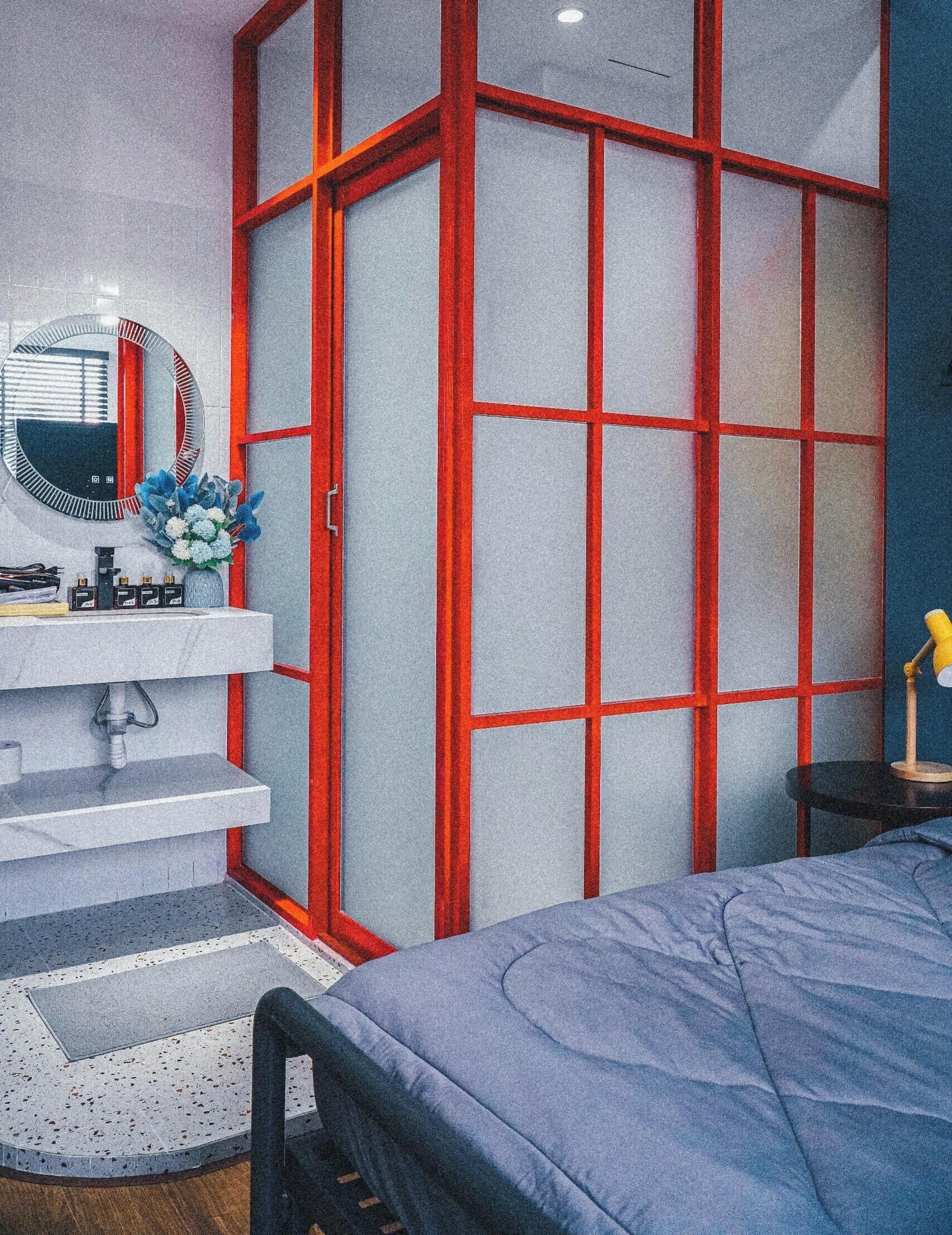 A bedroom with a bed, a bedside table, a mirror, and a red-framed partition.