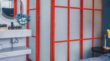 A bedroom with a bed, a bedside table, a mirror, and a red-framed partition.