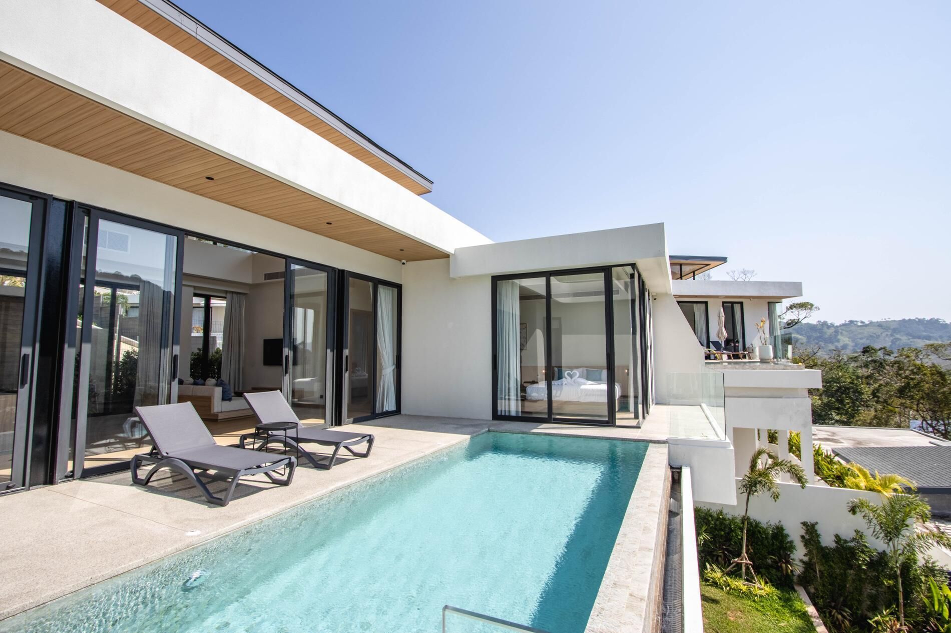 Une maison moderne dotée d’une piscine, de grandes portes vitrées et offrant une vue sur les collines.