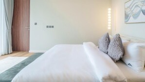 Un lit bien fait, avec des oreillers, un mur de couleur claire, un tableau et une porte avec des rideaux.