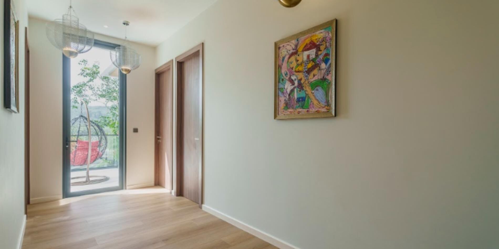 A hallway with a wooden floor, a glass door leading outside, and a colorful painting on the wall.