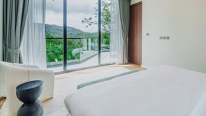 Une chambre dotée d’un grand lit, d’un canapé et offrant une vue sur un balcon agrémenté de verdure.