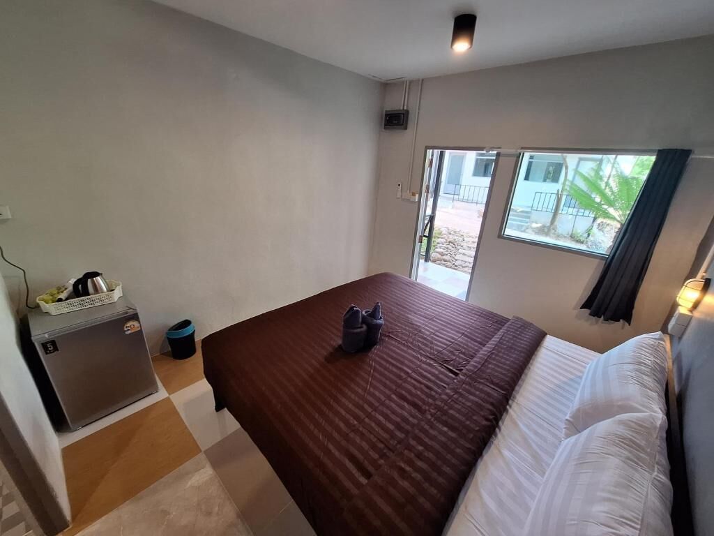 A bedroom with a bed, a small refrigerator, a window with curtains, and a door leading outside.