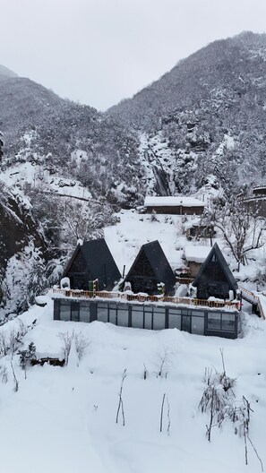 A snow-covered landscape with three cabins, each with a distinct roof design, surrounded by trees and a mountain backdrop.