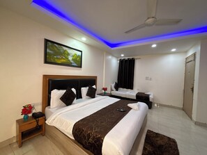 A hotel room with a large bed, a bedside table with a vase of flowers, a ceiling fan, and a painting on the wall.