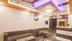 A modern lobby with a sofa set, a coffee table, a reception desk, a chandelier, and a ceiling fan. - HOTEL ROYAL RESIDENCY  (New Delhi)