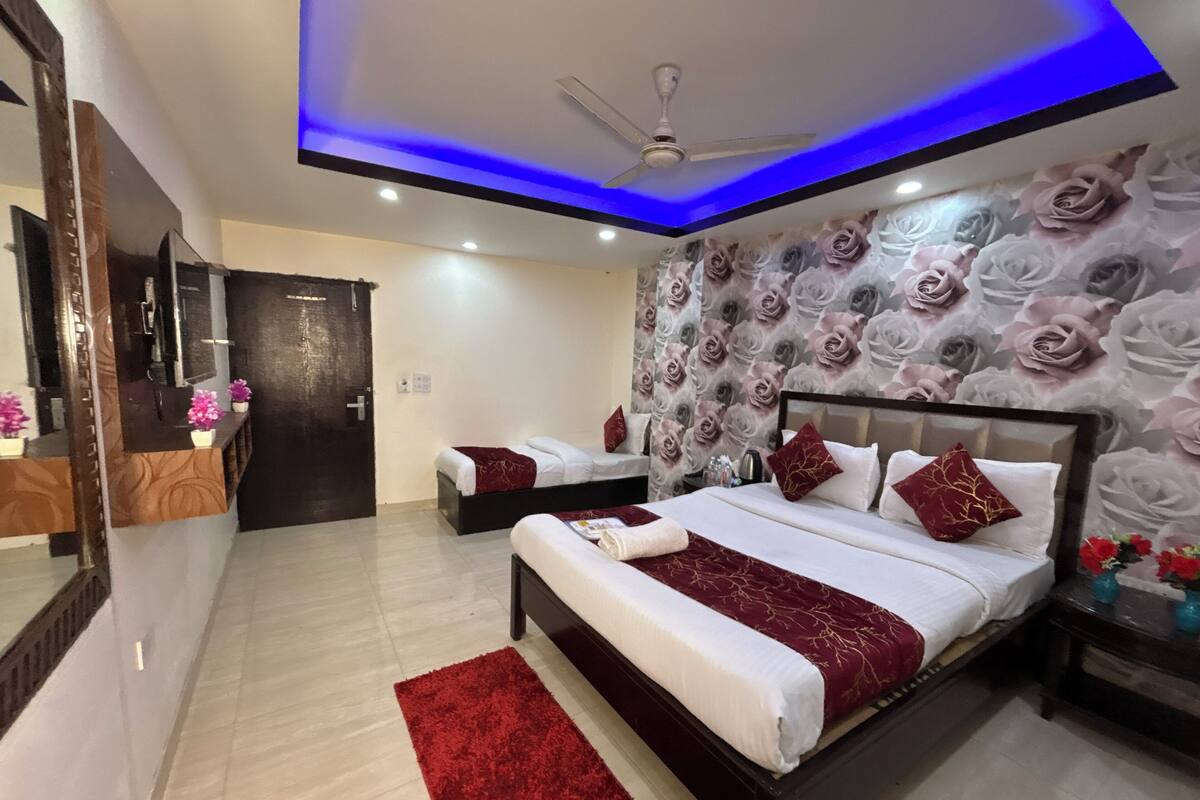 Habitación de hotel con una cama grande, una cama más pequeña, un ventilador de techo y una pared con estampado floral.