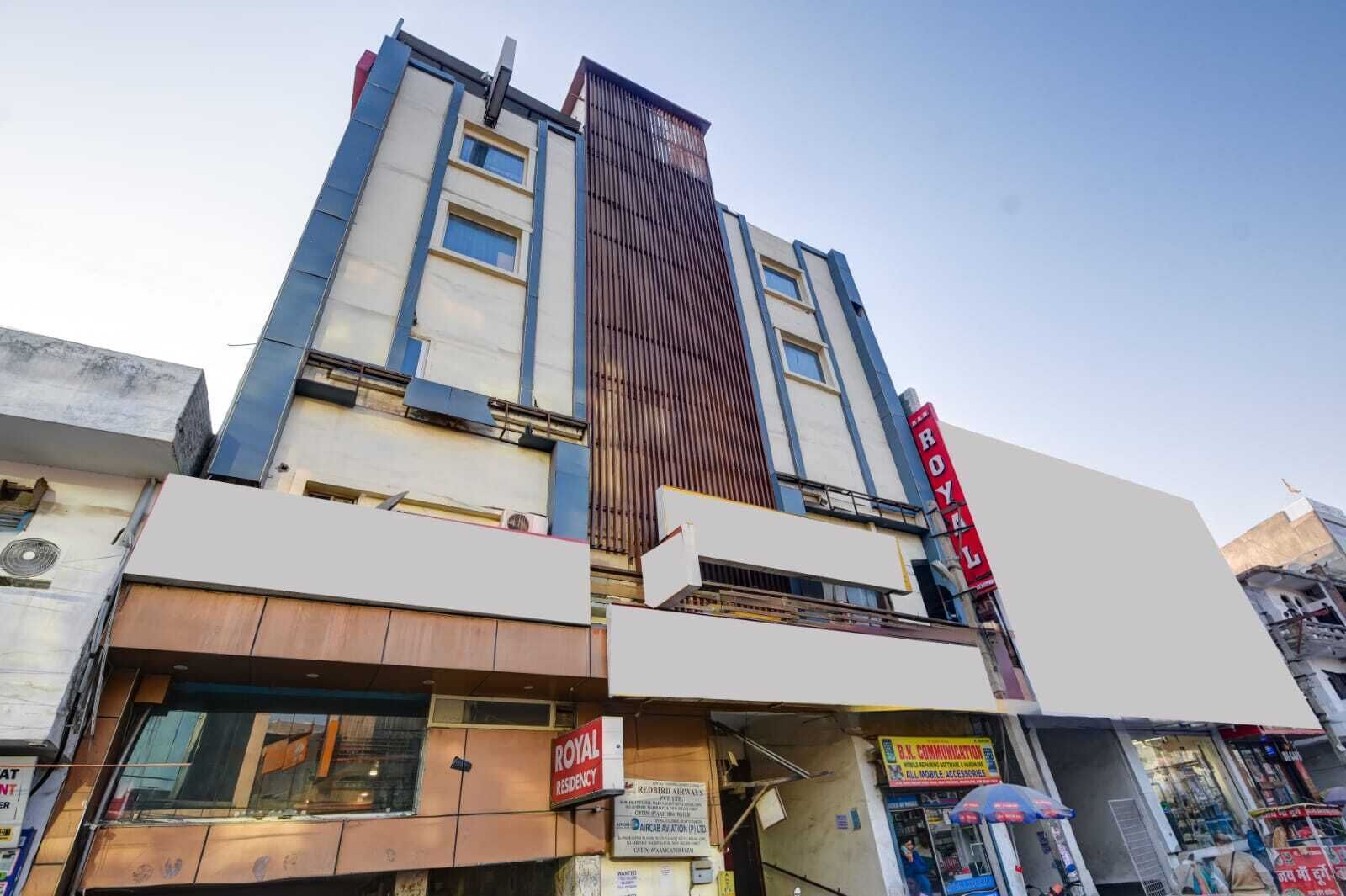A hotel with a prominent 'ROYAL RESIDENCY' sign, a modern facade, and a visible ground floor with various shops.