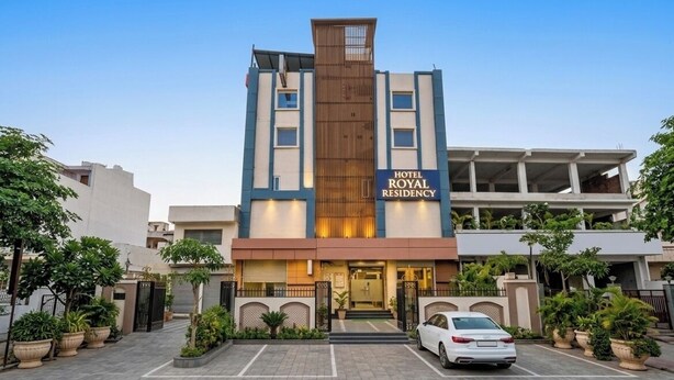 A hotel named 'Hotel Royal Residency' with a modern design, featuring a central vertical wooden panel, multiple floors, and a parking area with potted plants. - HOTEL ROYAL RESIDENCY  (New Delhi)