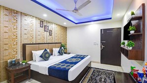 A modern hotel room with a bed, a ceiling fan, a dark door, and a shelf with plants. - HOTEL ROYAL RESIDENCY  (New Delhi)