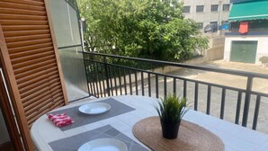 A balcony with a table set for dining, a potted plant, and a view of a building and trees. - Ayres, Simple Apartment (El Vendrell)