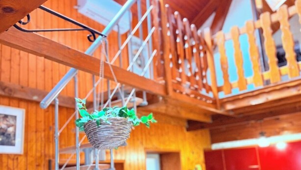 A wooden interior with a hanging basket, a staircase, and a kitchen area.