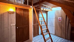 A loft bedroom with a wooden ladder, a door, and a light fixture.