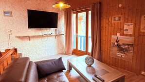 A cozy living room with a leather sofa, a wooden coffee table, a mounted TV, and a wooden ceiling.