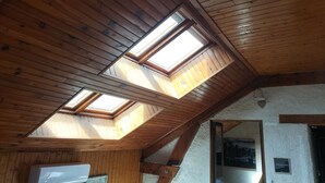 A room with wooden ceiling beams, skylights, and a white textured wall.