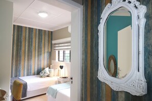 A bedroom with a bed, bedside table, lamp, and a mirror on the wall. - 7 Sands (Ballito)