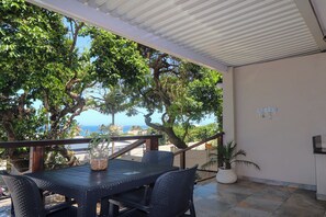 Une terrasse extérieure avec une table et des chaises, entourée d’arbres et offrant une vue sur la mer.