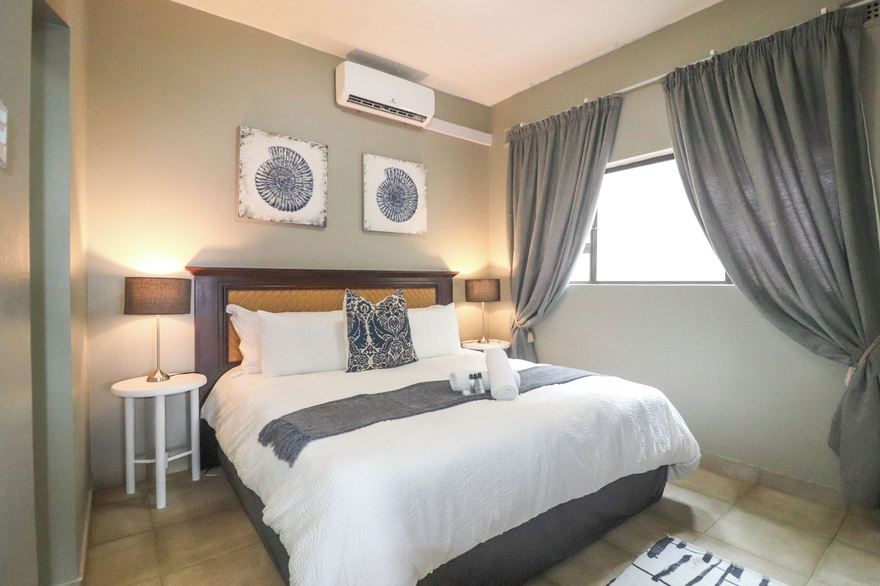 Ein Hotelzimmer mit einem Bett, zwei Nachttischlampen, einem Vorhangfenster und einer Klimaanlage.