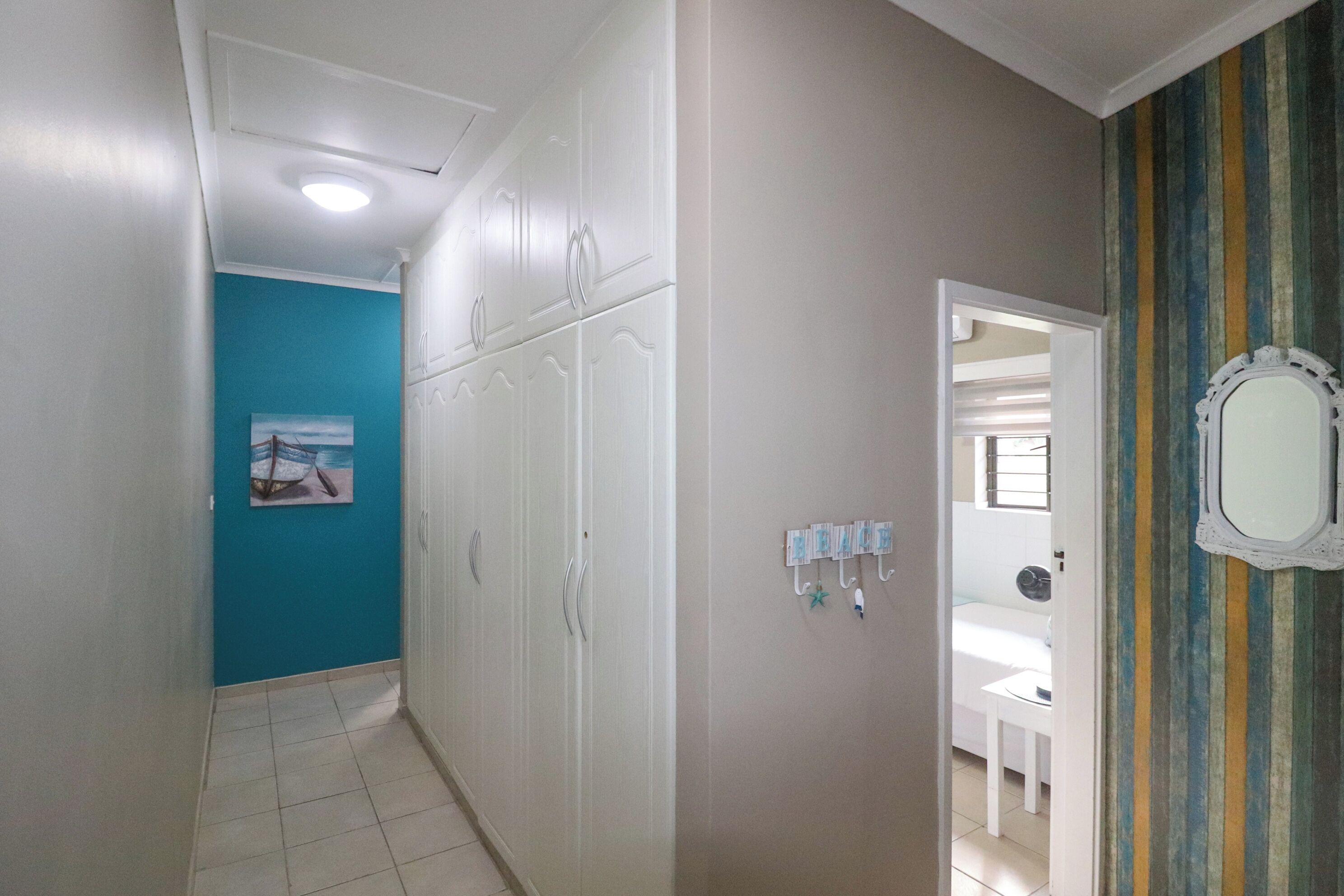 A hallway with a white wardrobe, a blue wall, and a door leading to a bathroom.