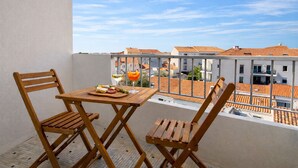 Een balkon met een tafel en twee houten stoelen, een glas witte wijn en een glas sinaasappelsap.