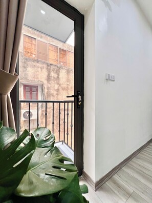 A room with a sliding glass door leading to a balcony, a potted plant, and a wall-mounted light switch. - Aurora Homestay 16 Nguyen Nhu Do (Hanoi)