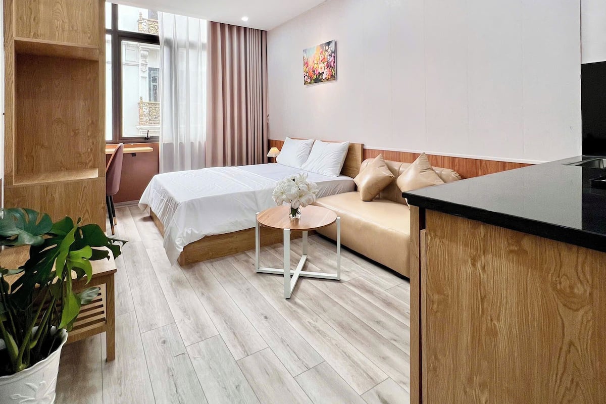 A modern hotel room with a bed, sofa, dining table, and a potted plant.
