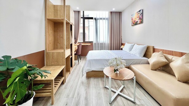 Et hotelværelse med seng, sofa, skrivebord, stol, en potteplante og et vindue med gardiner.