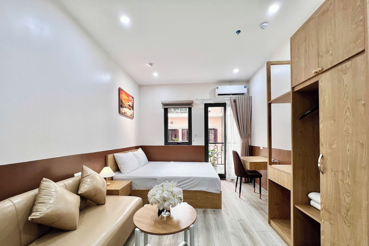 A hotel room with a bed, a sofa, a small table with flowers, a desk, and a wardrobe.