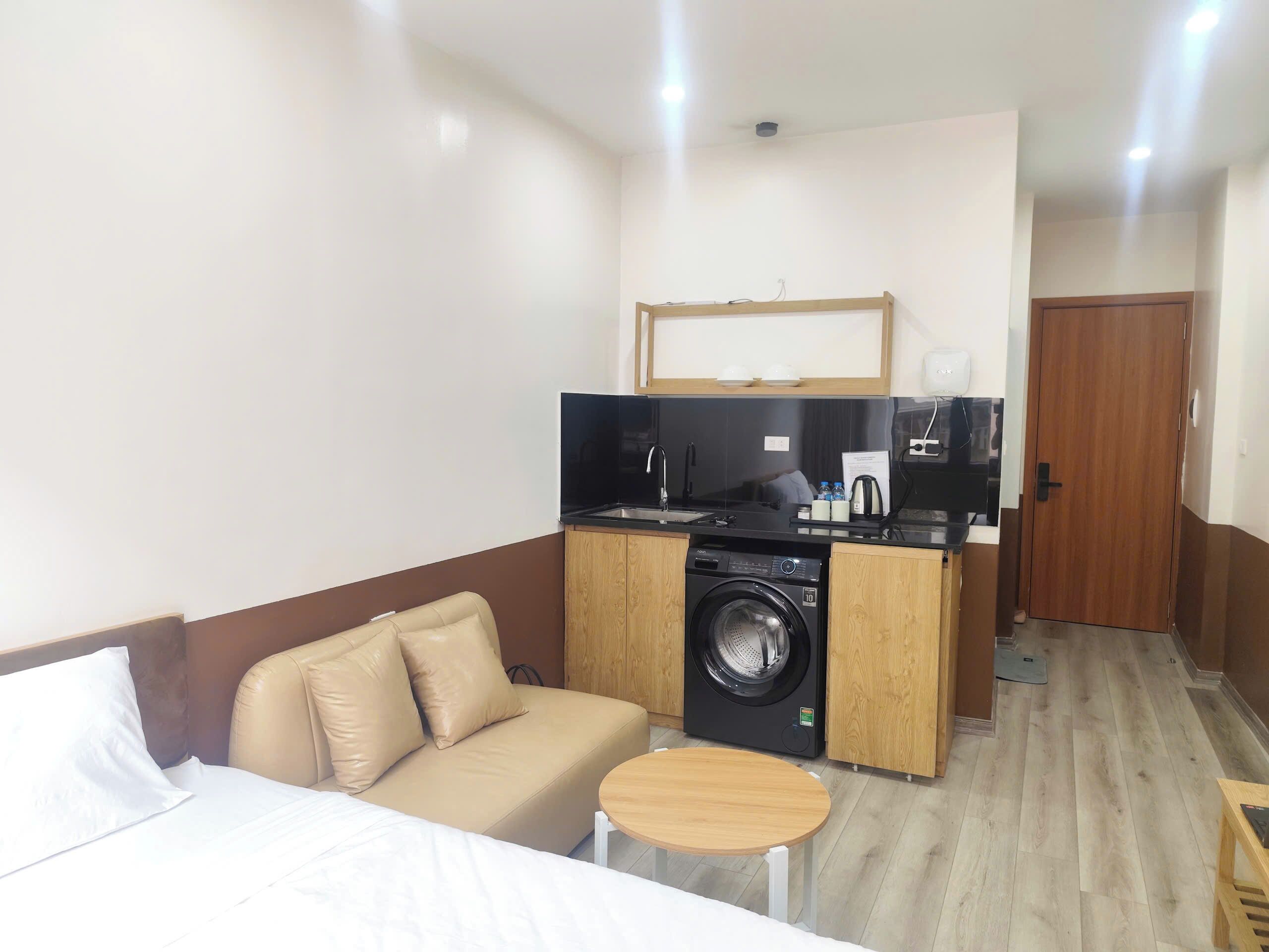 Camera d'albergo compatta con un letto, un divano, un tavolino, una lavatrice e angolo cottura.