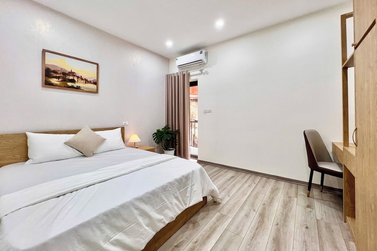 A bedroom with a bed, bedside lamp, potted plant, and a desk with a chair.
