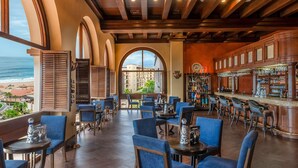 Ein Restaurant mit Blick auf den Strand, das blau gepolsterte Stühle, eine Bar und ein großes Bogenfenster bietet.