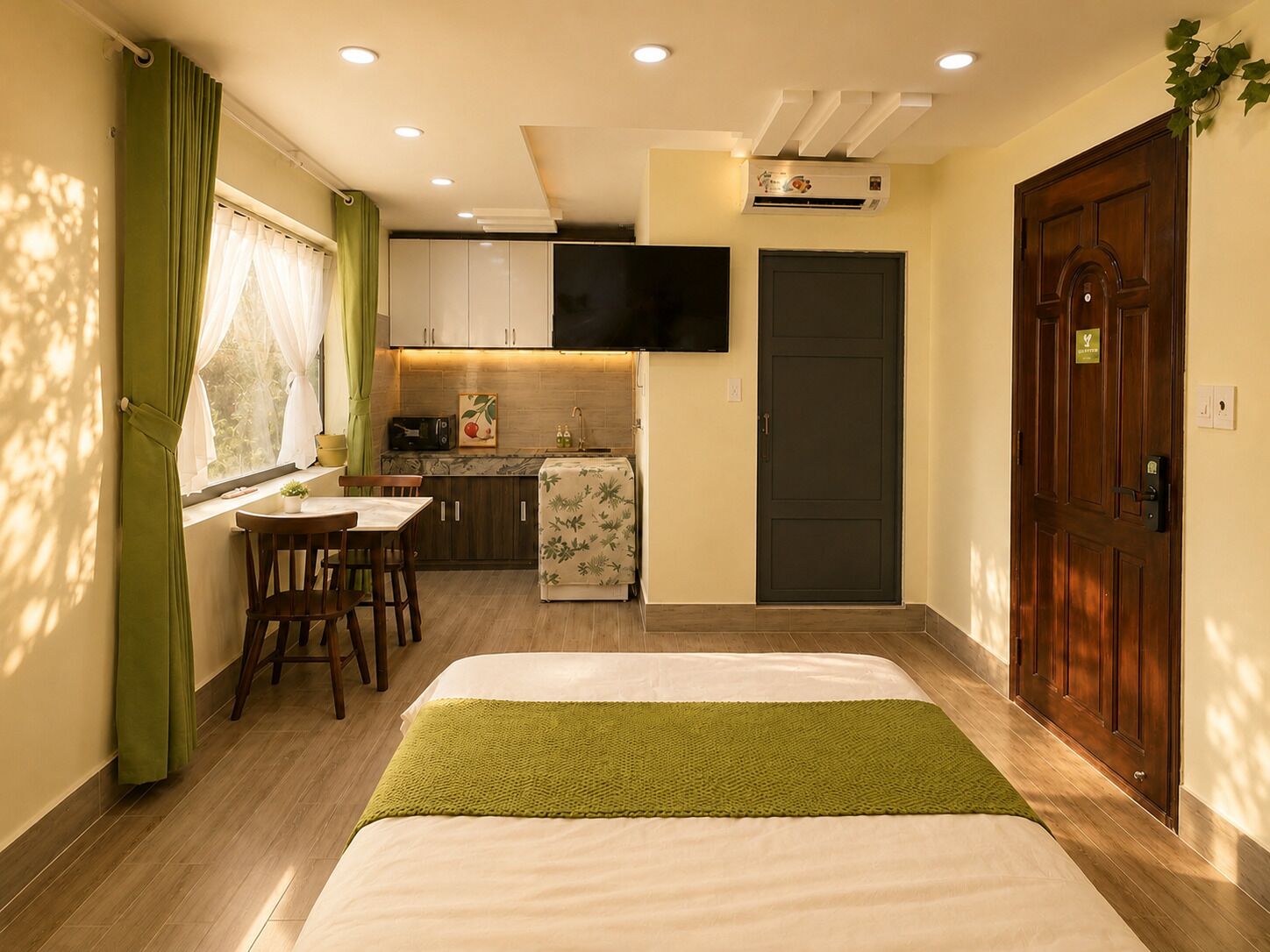 A compact hotel room with a bed, a small kitchenette, a dining area, and a door.