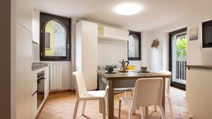 A kitchen with white cabinets, a stove, and a dining area with two chairs and a table. - Lemon House 2 by Wonderful Italy (Gardone Riviera)
