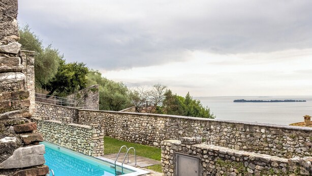 A stone pool with a view of the sea, surrounded by stone walls and a grassy area. - Lemon House 2 by Wonderful Italy (Gardone Riviera)