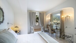 Habitación de hotel con cama, escritorio, silla, lámpara, espejo y vista a un balcón.