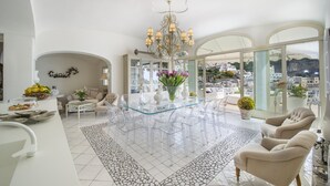 Amplia sala de estar con una mesa de comedor de vidrio rodeada de sillas, un candelabro y vistas a la ciudad.