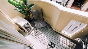 A small balcony with a chair, a potted plant, a pair of shoes, and a radiator.