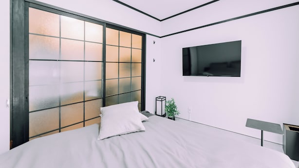 A bedroom with a bed, a TV mounted on the wall, and a sliding glass door.