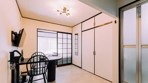 A room with a dining table, chairs, a black coffee machine, a window with blinds, and a wardrobe.