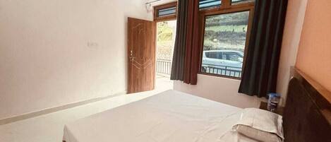 A bedroom with a bed, a window with curtains, a door, and a view of a car outside.