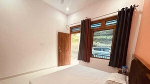 A bedroom with a large bed, a window with curtains, a door, and a view of a car outside. - Hotel Moon Rise (Ukhimath)