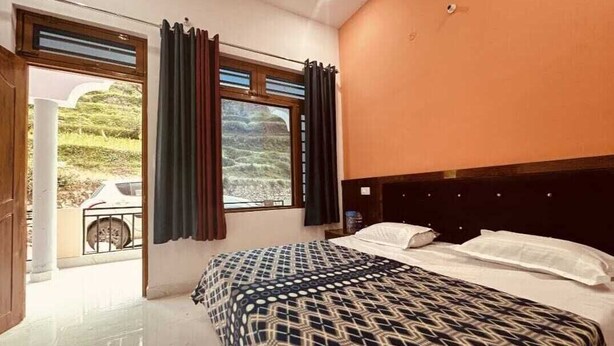 A bedroom with a bed, a window with curtains, and a view of a landscape. - Hotel Moon Rise (Ukhimath)