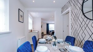 Un coin repas avec une table dressée pour six personnes, des chaises bleues et une cuisine en arrière-plan.