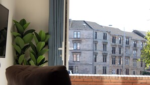 Ein Zimmer mit braunem Ledersessel, einer Topfpflanze und Blick auf eine Ziegelwand und Gebäude.
